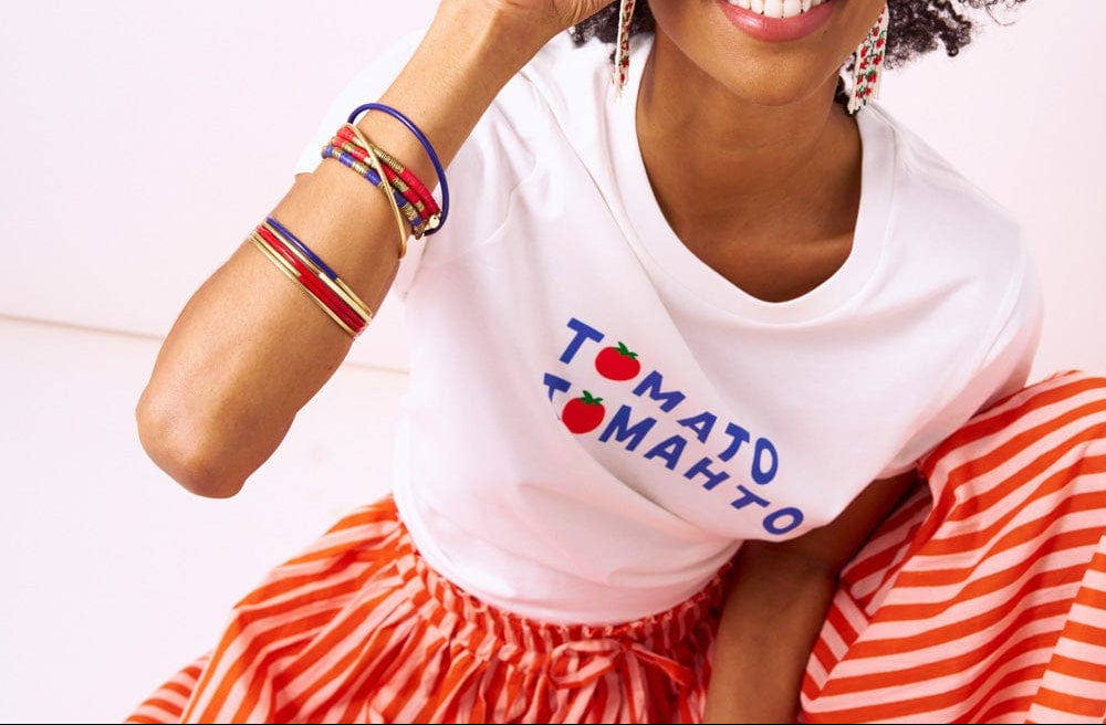 Woman holding a cherry tomato up to her eye, wearing a 'Tomato Tomato' shirt.