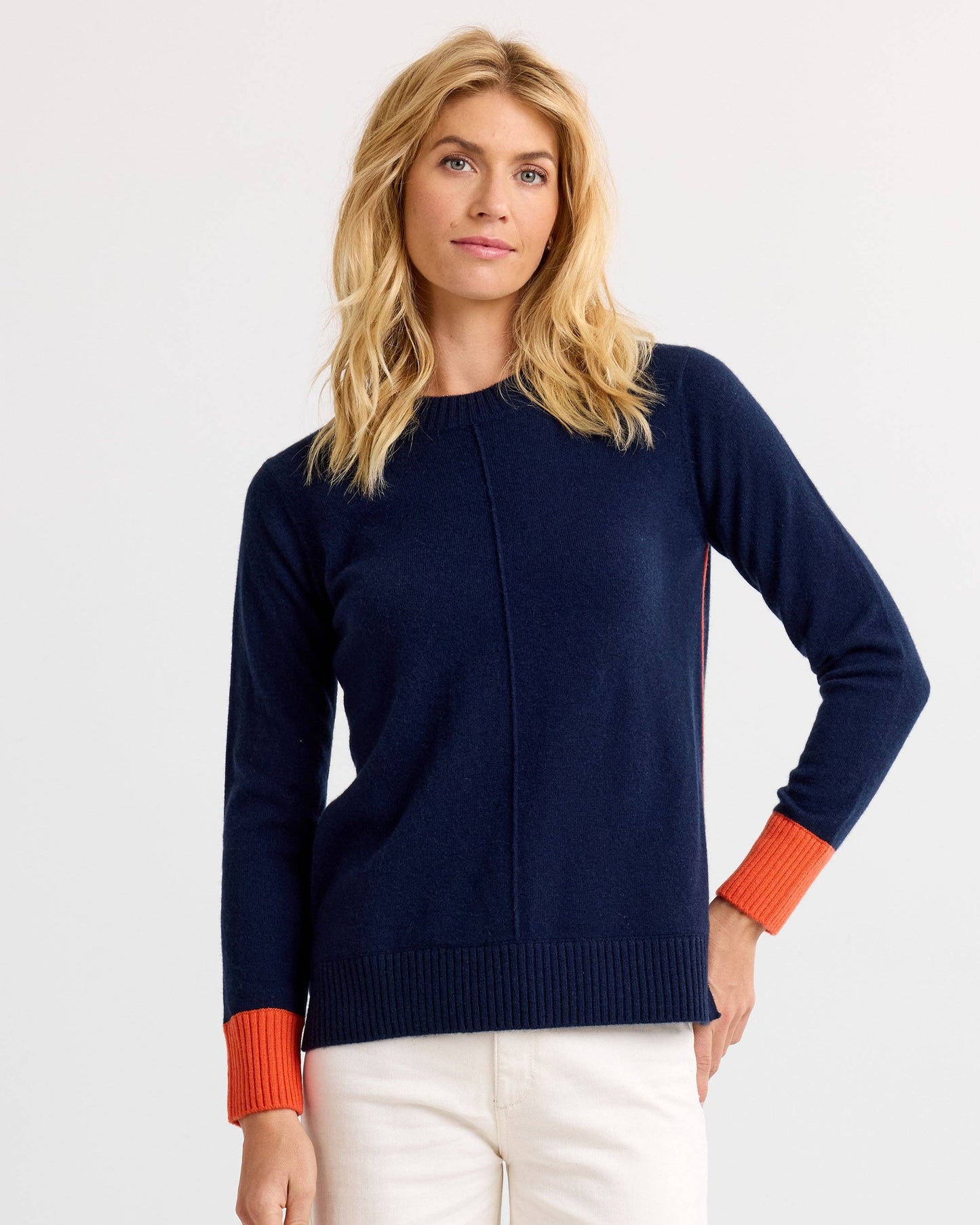 Woman wearing a navy sweater with orange cuffs and hem on a light gray background