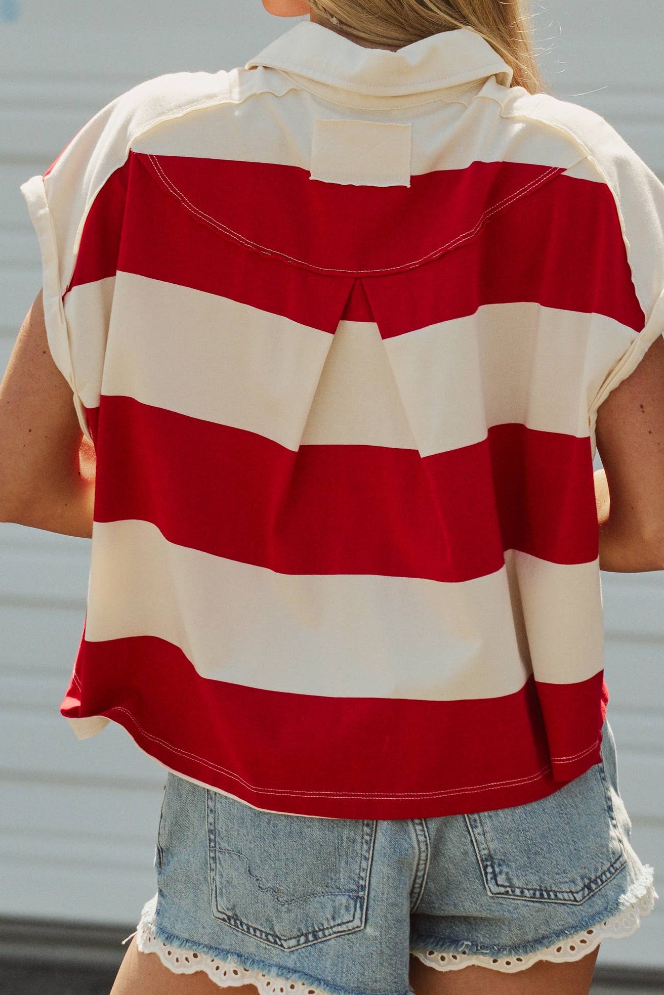 Person wearing a red and white striped shirt with denim shorts against a plain background
