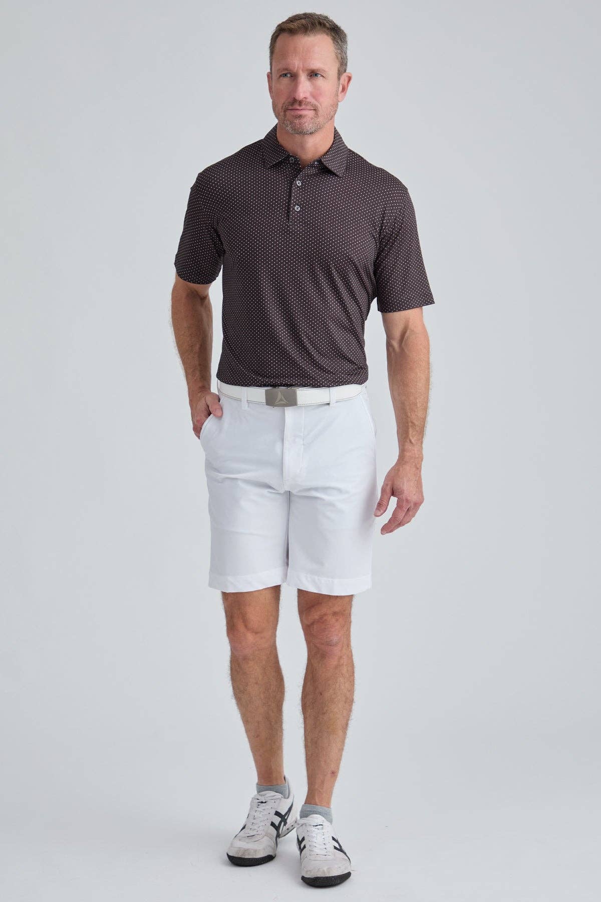 Man wearing a brown patterned polo shirt and white shorts on a light gray background