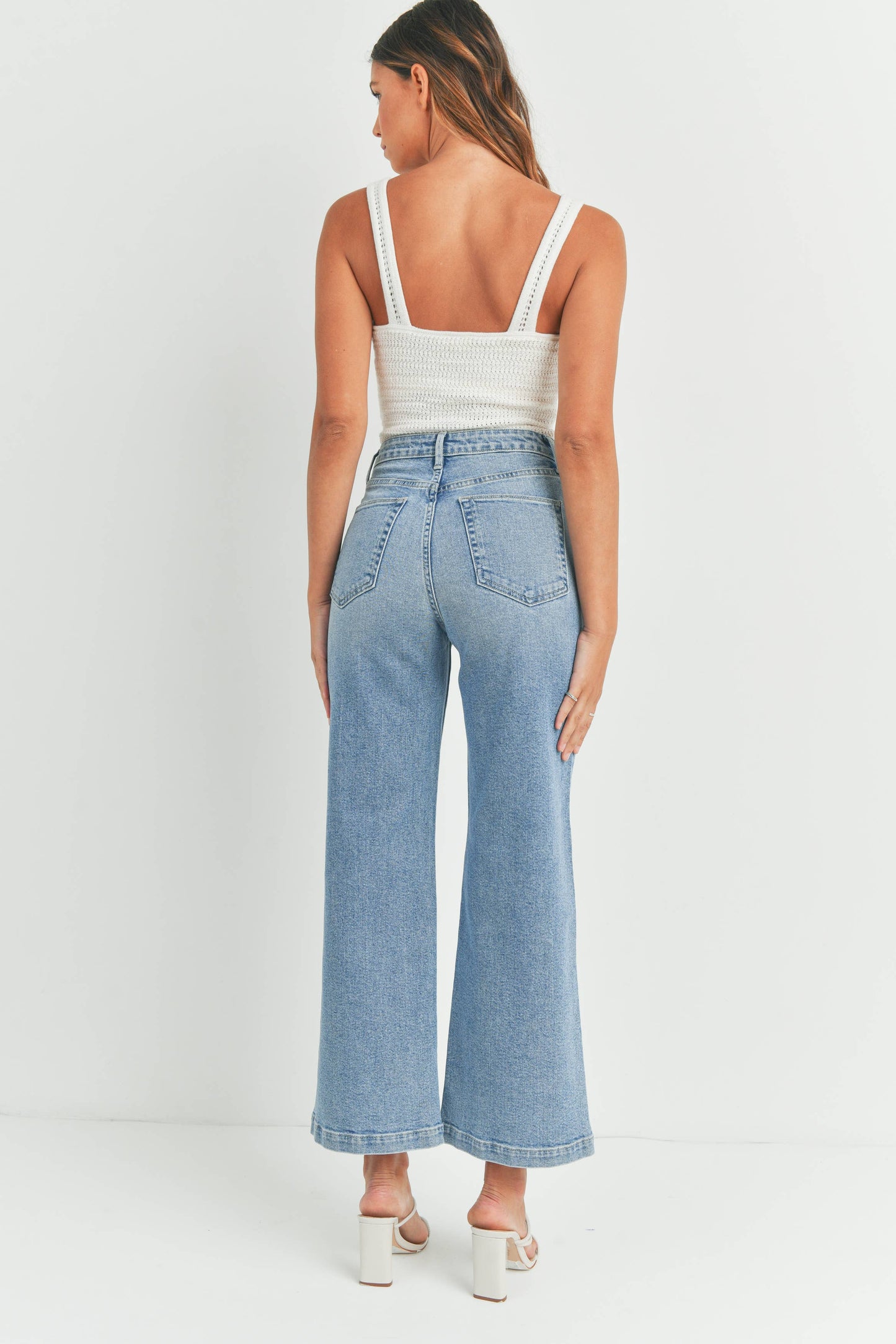 Woman wearing a white tank top and light blue jeans on a white background