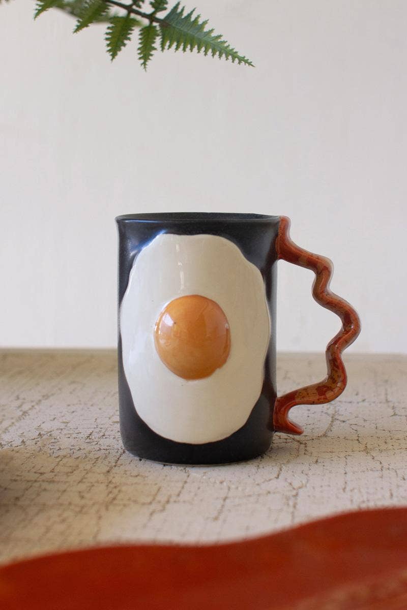 Mug with a design of a fried egg on a wooden surface with a plant in the background