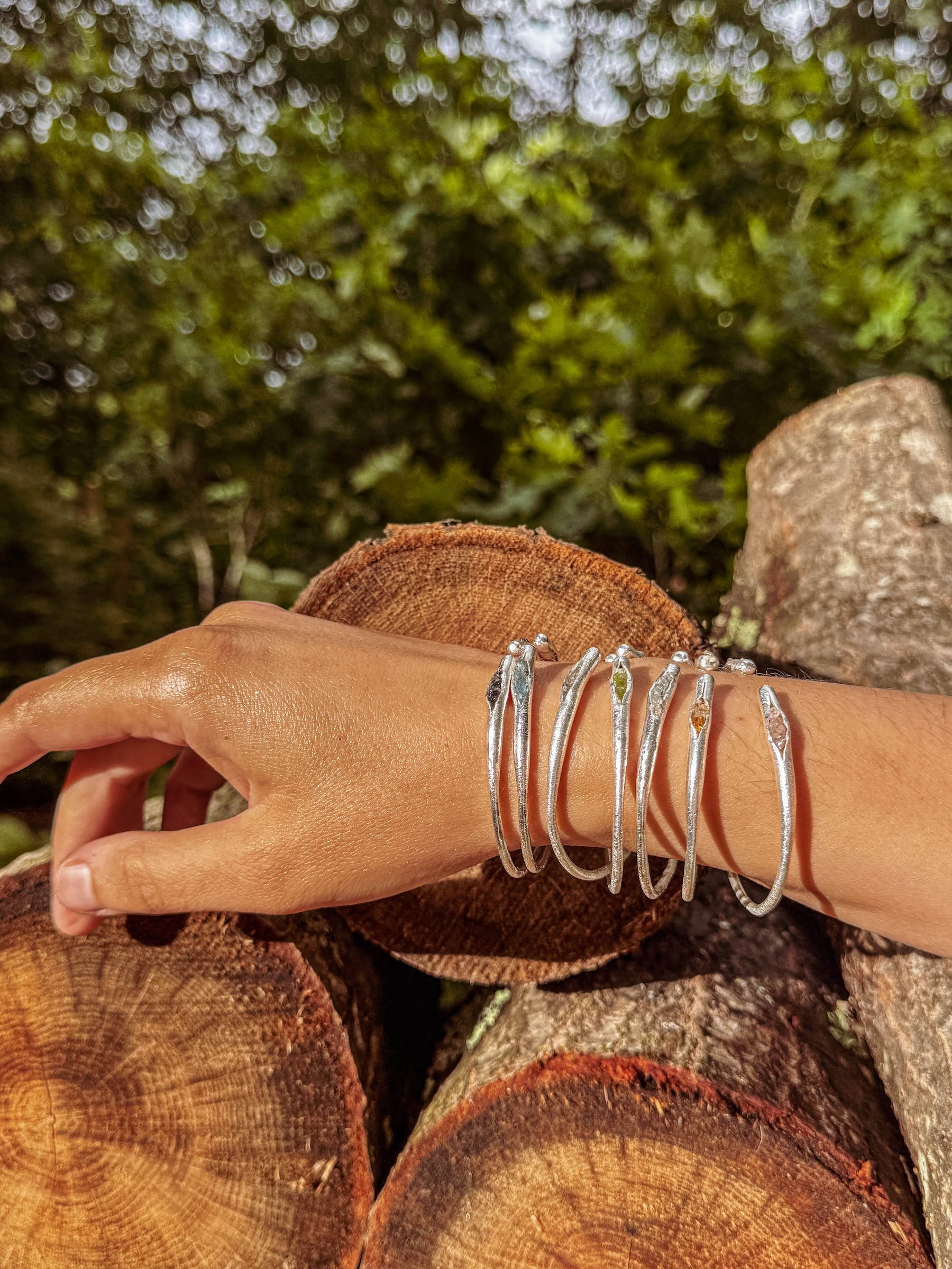 Hand wearing multiple silver bracelets on a wooden log with a natural background