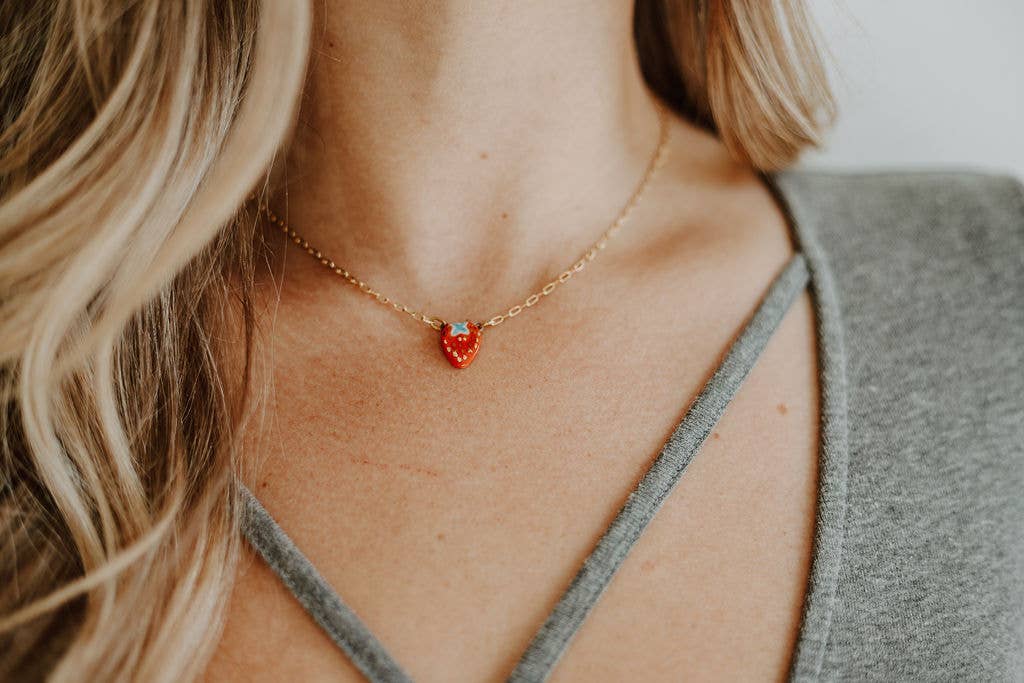 Person wearing a gold necklace with a red heart pendant.