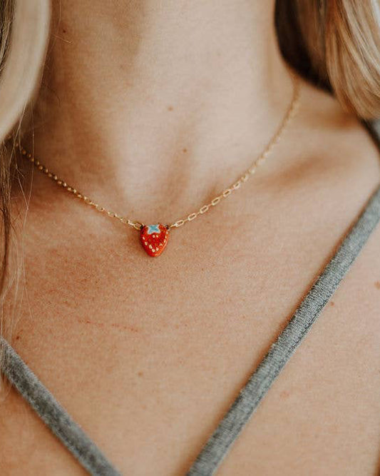 Person wearing a gold necklace with a red heart pendant.