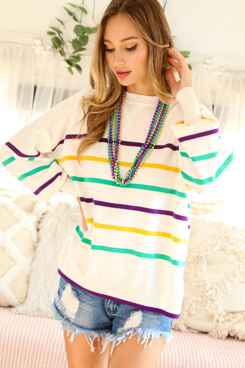 Woman wearing a white sweater with colorful stripes and denim shorts indoors.