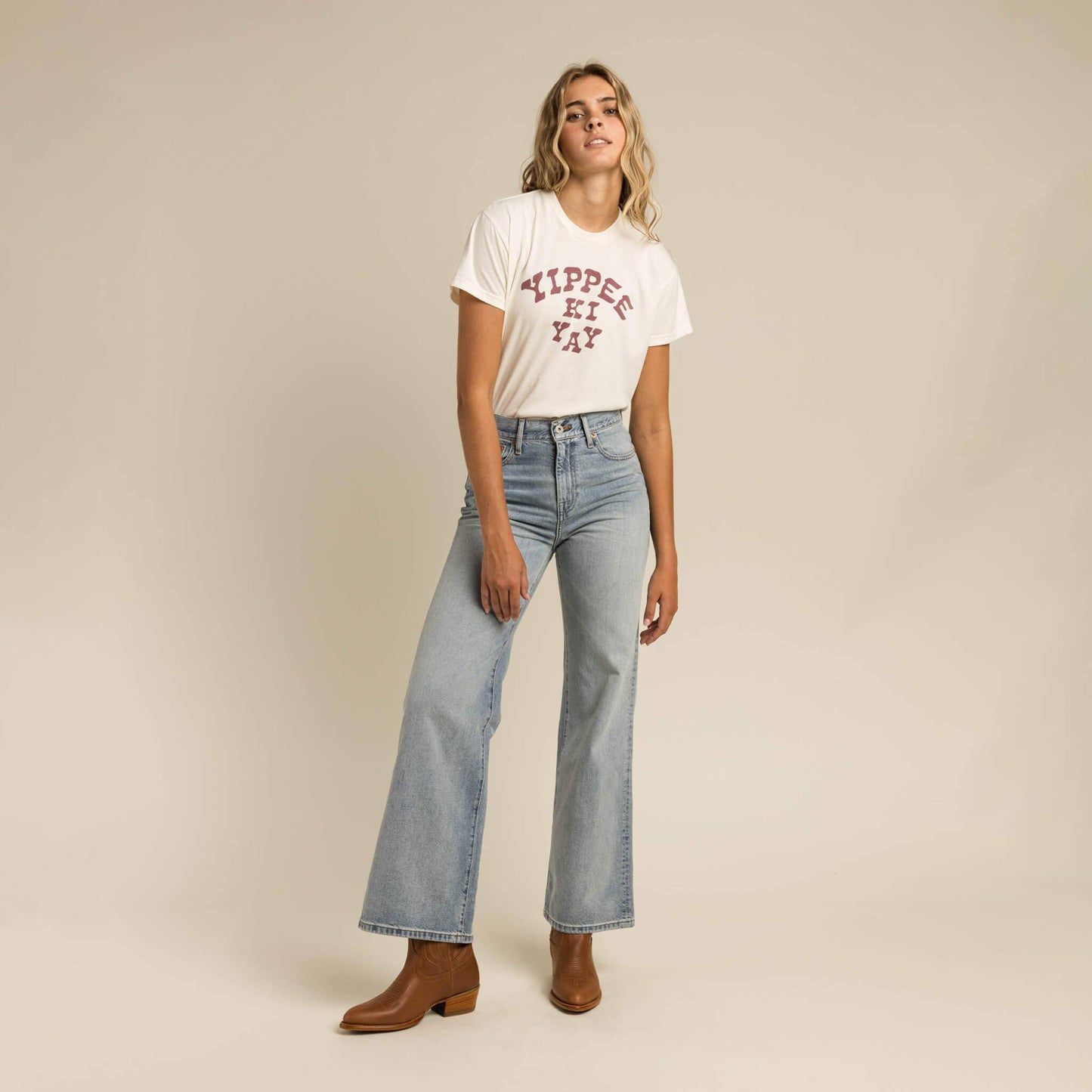 Woman wearing a white t-shirt with text and blue jeans on a beige background