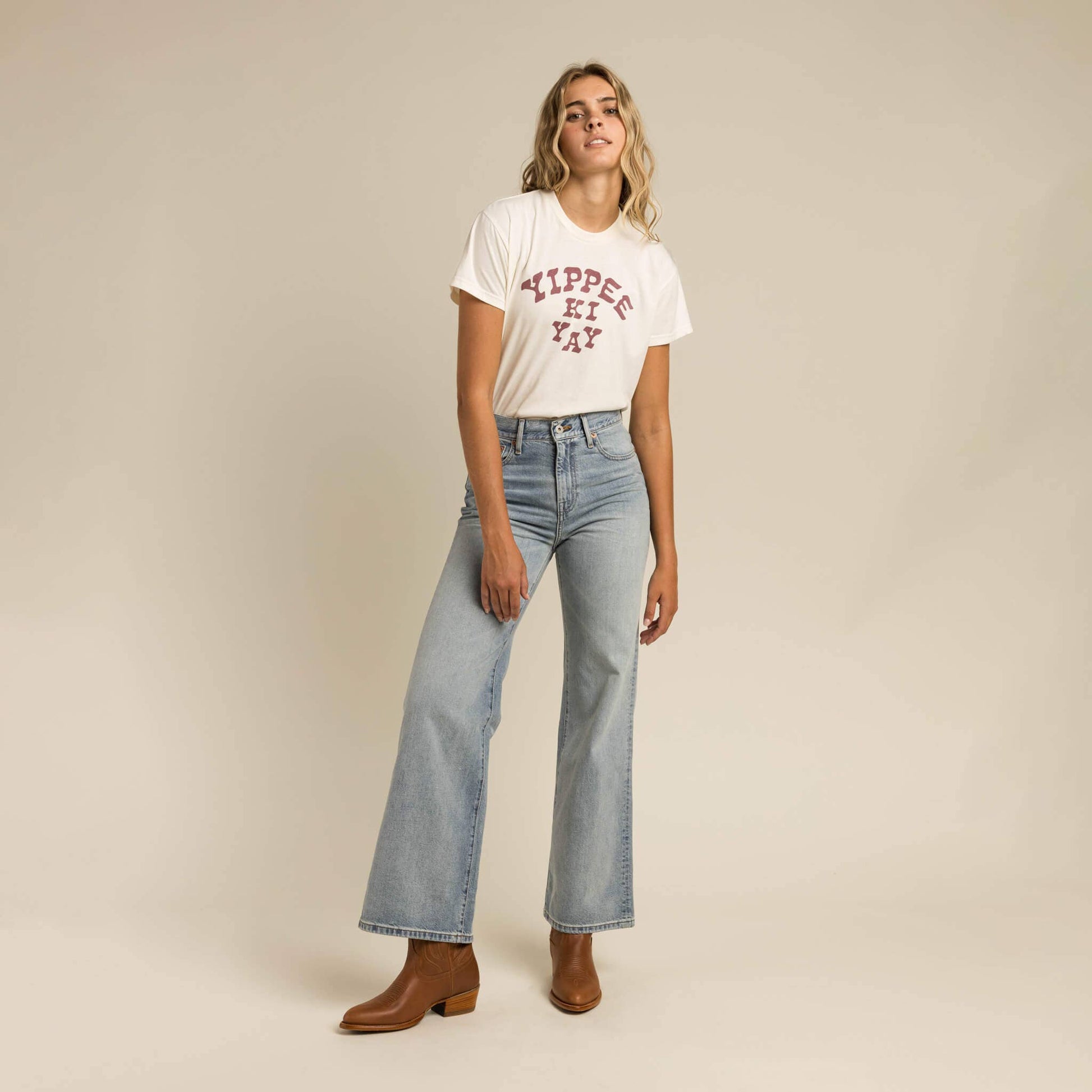 Woman wearing a white t-shirt with text and blue jeans on a beige background