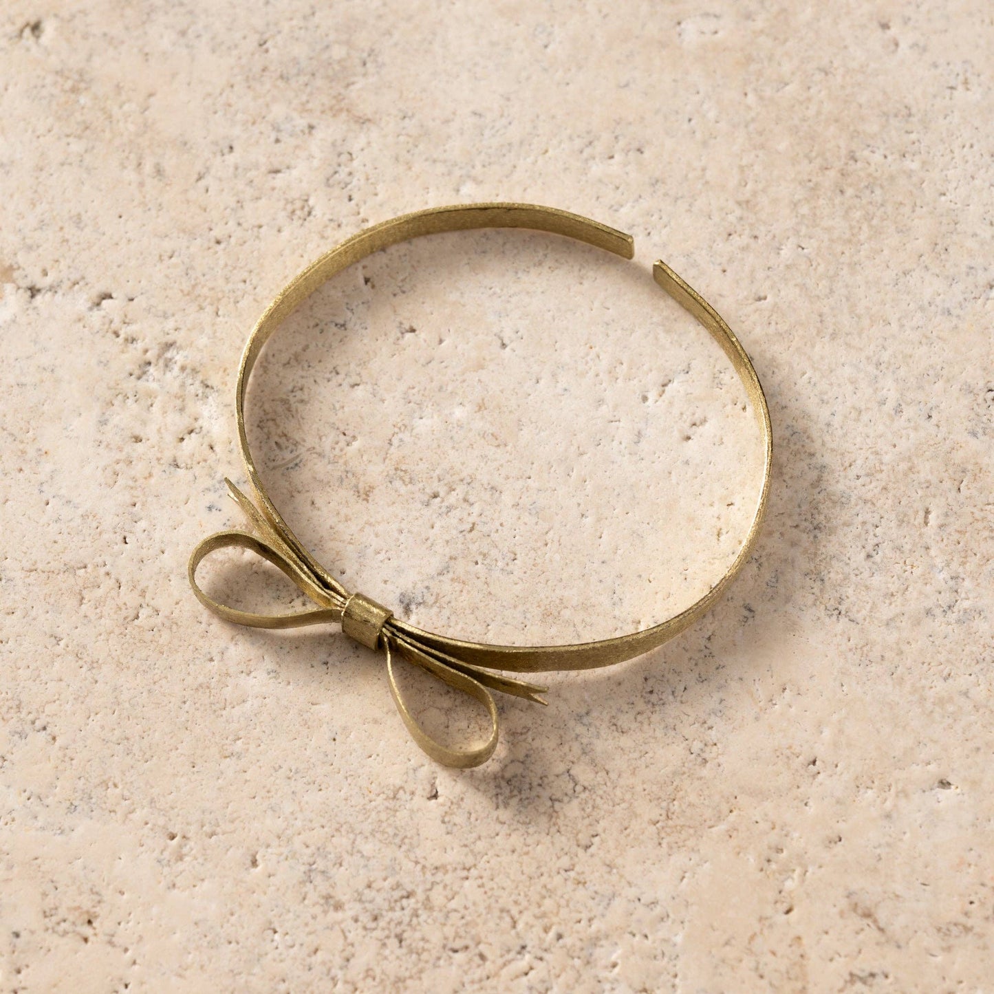 Brass bracelet with a bow on a textured beige surface