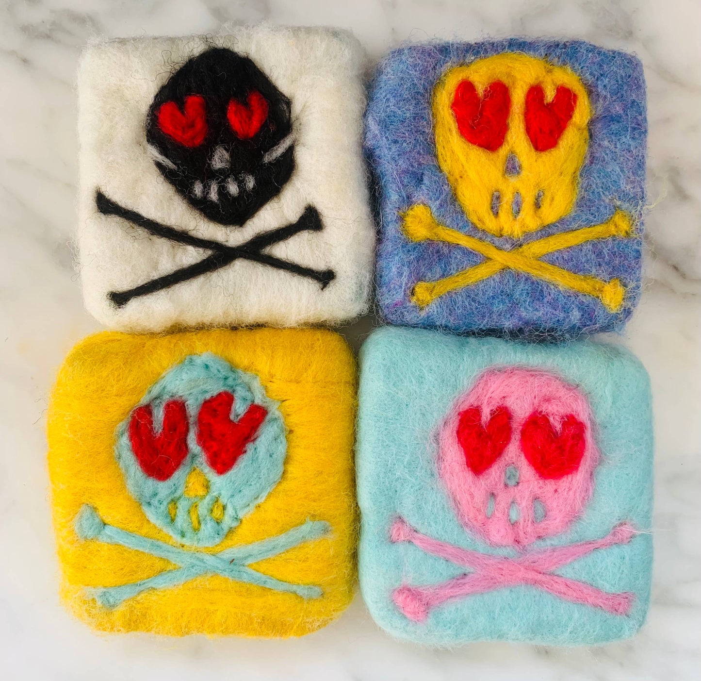 Four colorful square patches with skull and crossbones designs on a marble surface.