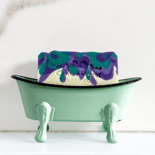Bar of soap with purple and green swirls in a green bathtub-shaped holder on a white background