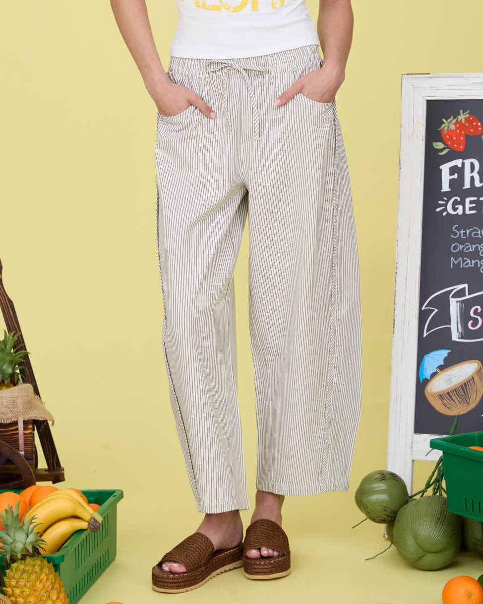 Woman wearing a sleeveless shirt with fruit graphics and text, standing in front of a yellow wall with produce and a chalkboard sign.
