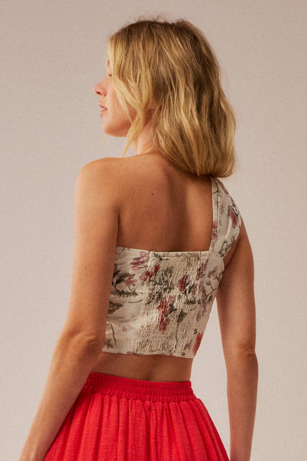 Woman wearing a floral top and red skirt against a plain background