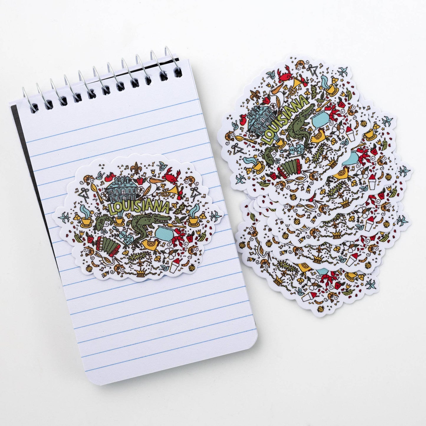 Notebook with decorative Louisiana-themed cover and matching sticker on a white background