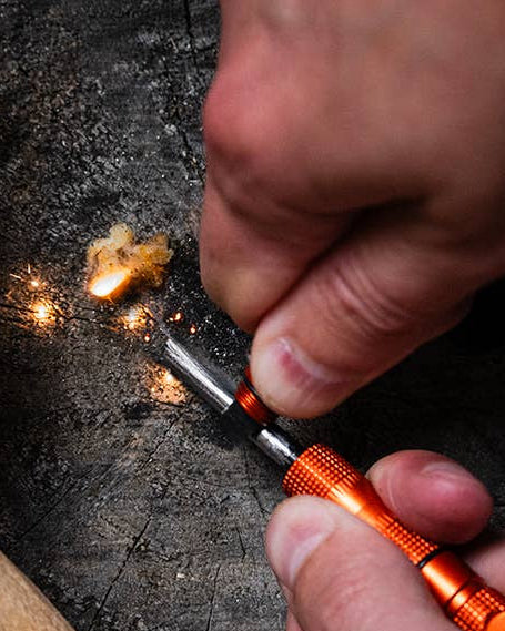 Person using a Lucky Jack fire starter to ignite wood on a rustic surface.