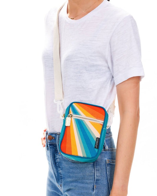 Person wearing a colorful crossbody bag with a white shirt and blue jeans.