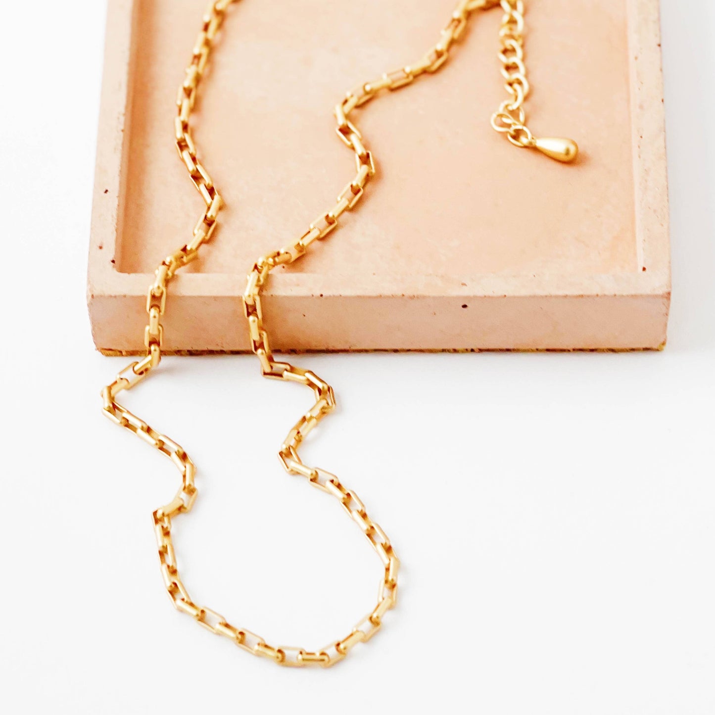 Gold chain necklace on a white surface with a wooden box in the background