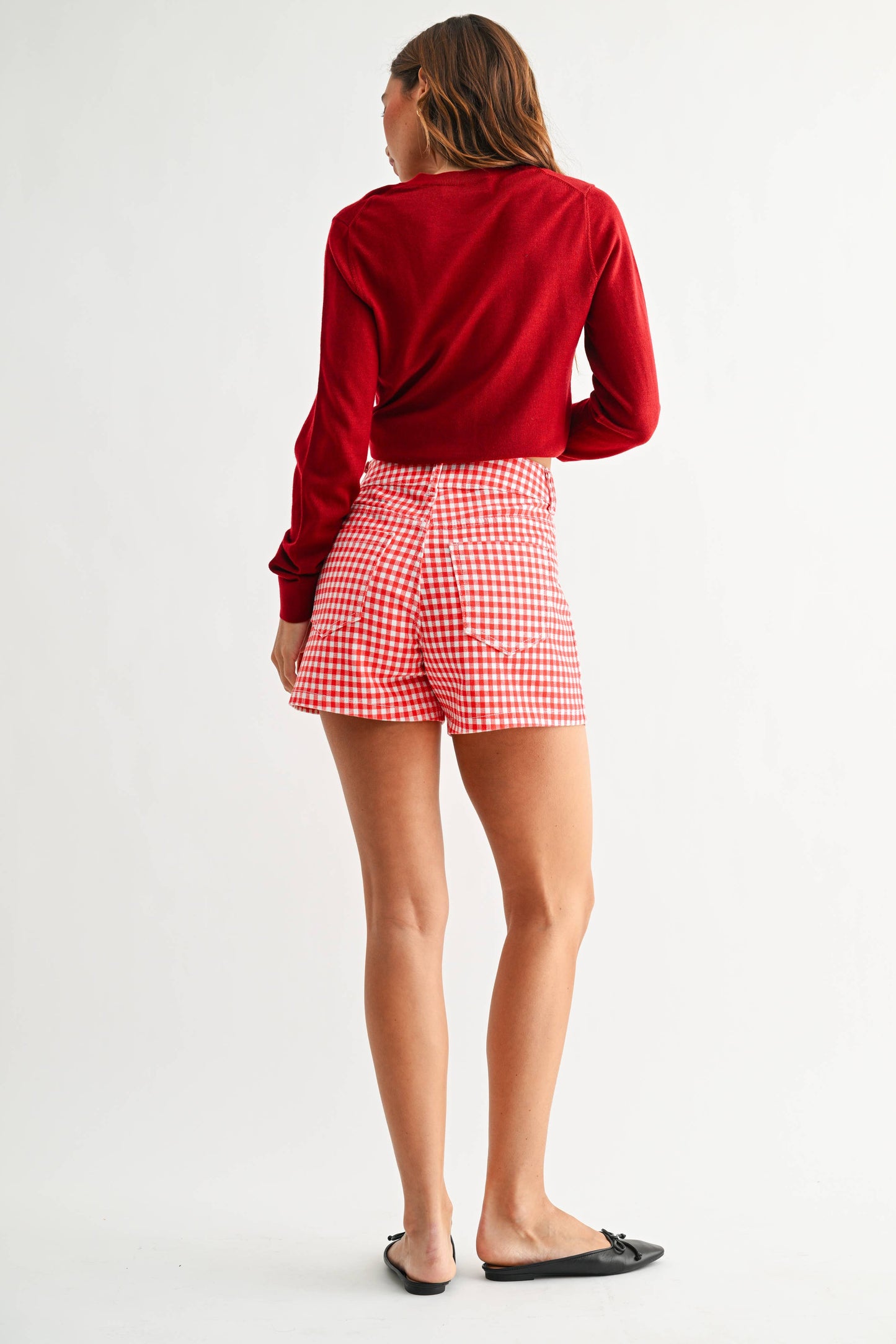 Person wearing a red long-sleeve top and red checkered shorts on a white background