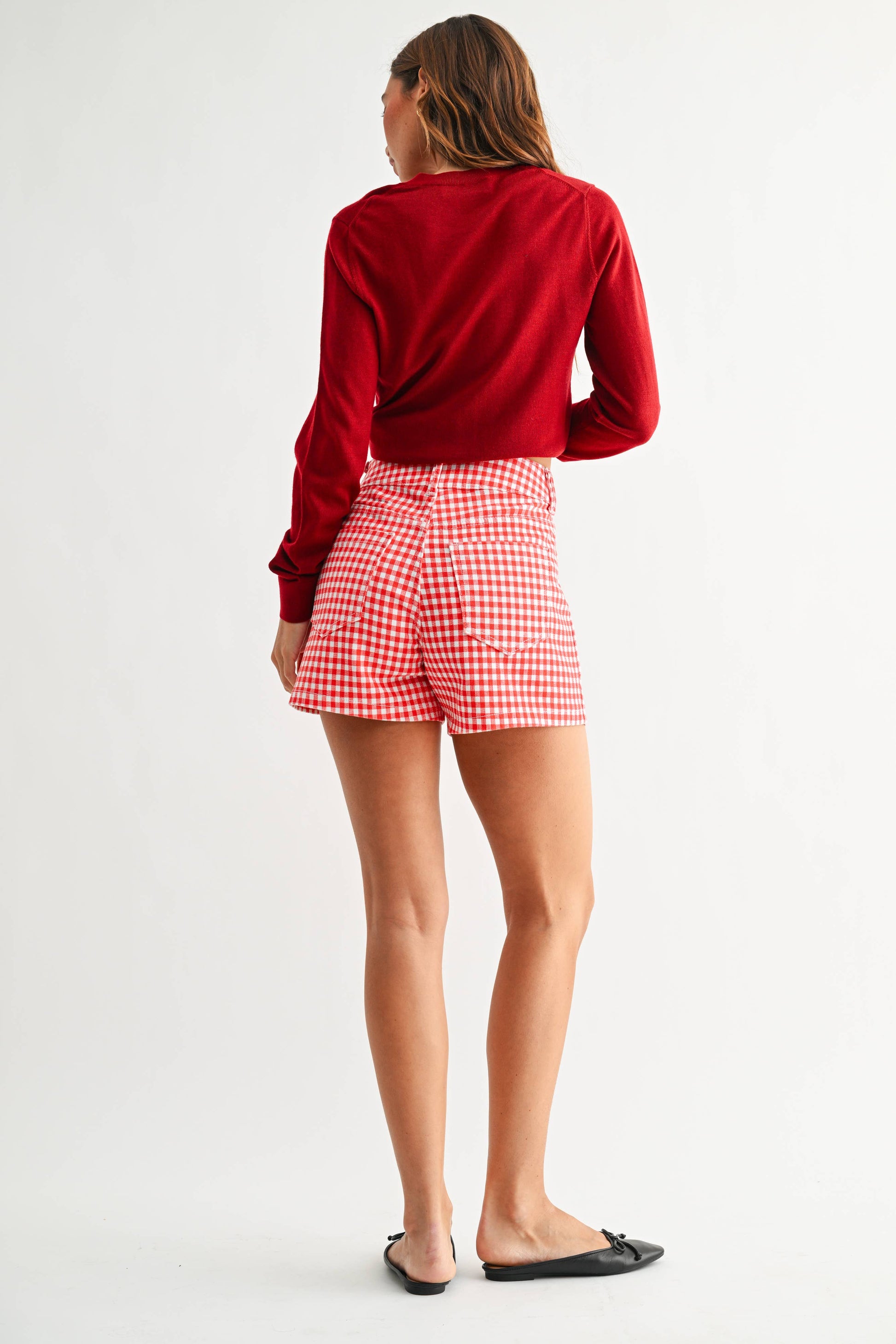 Person wearing a red long-sleeve top and red checkered shorts on a white background
