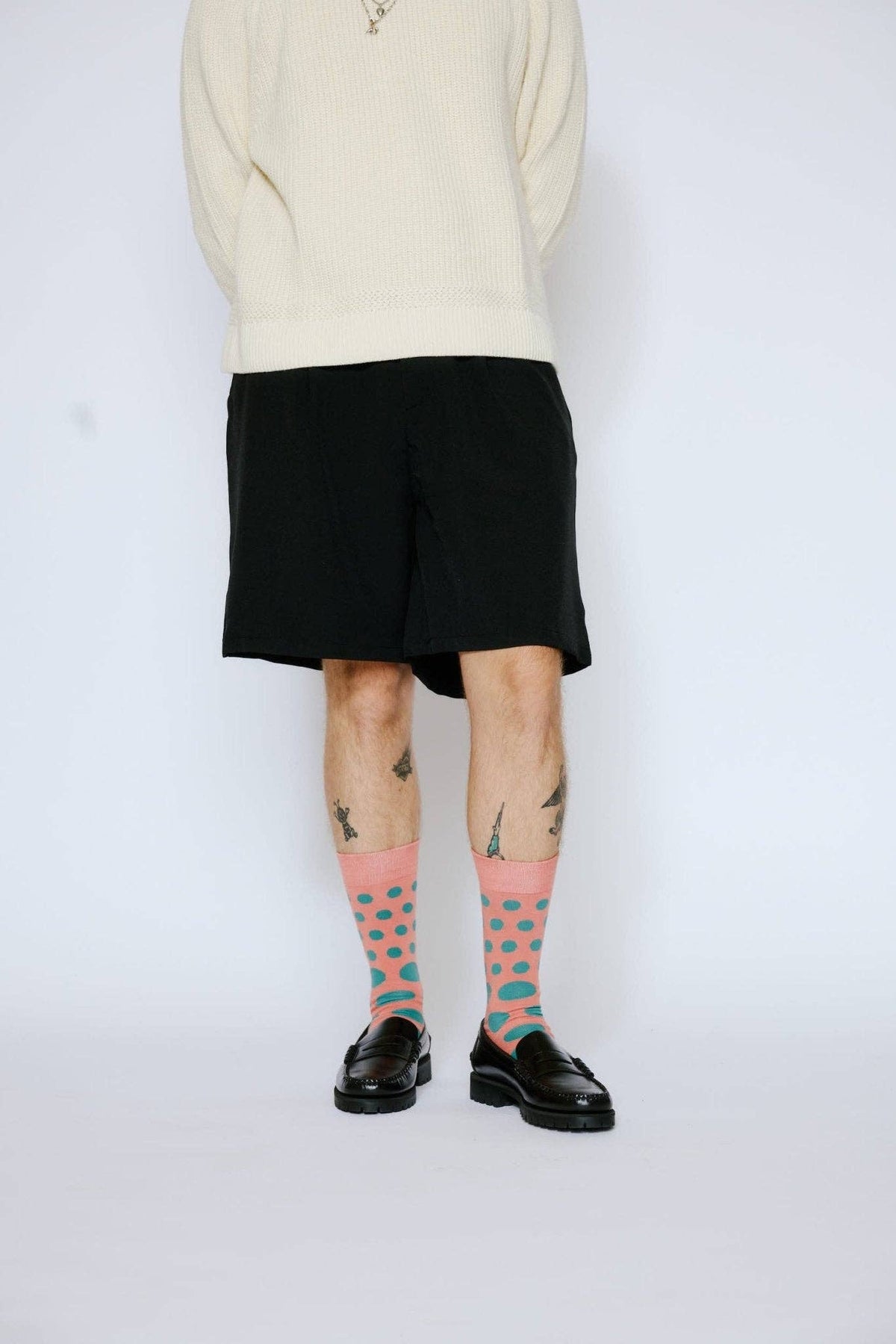 Person wearing a beige sweater, black shorts, and patterned socks on a white background
