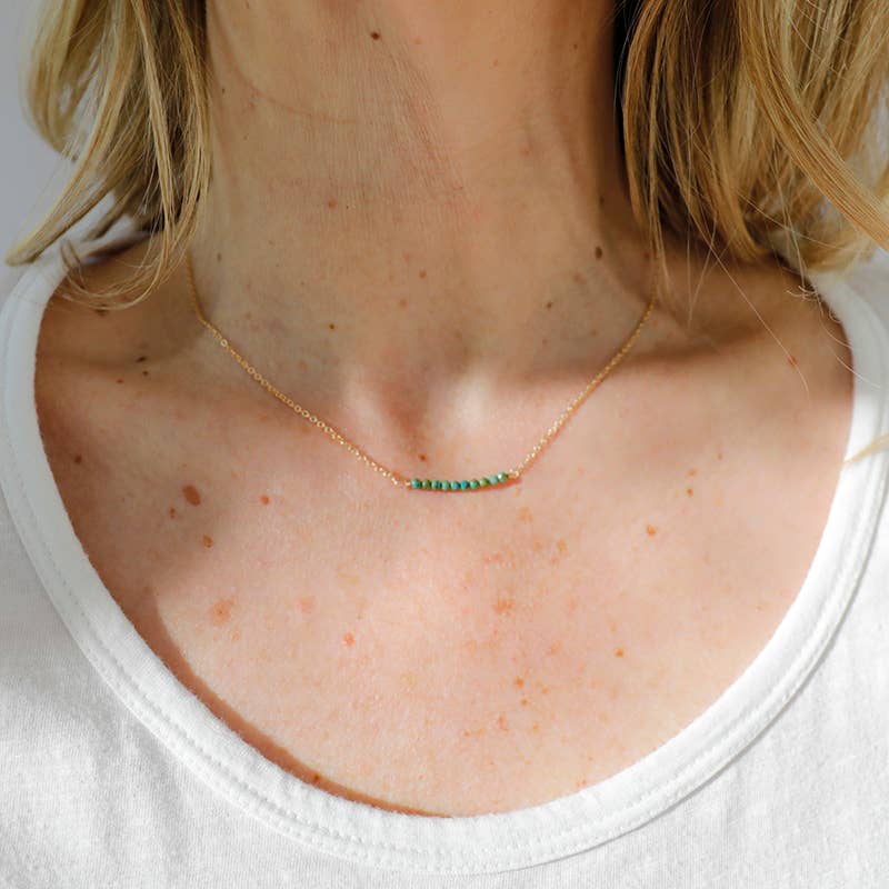 Necklace with green beads worn by a person with blonde hair, wearing a white shirt.