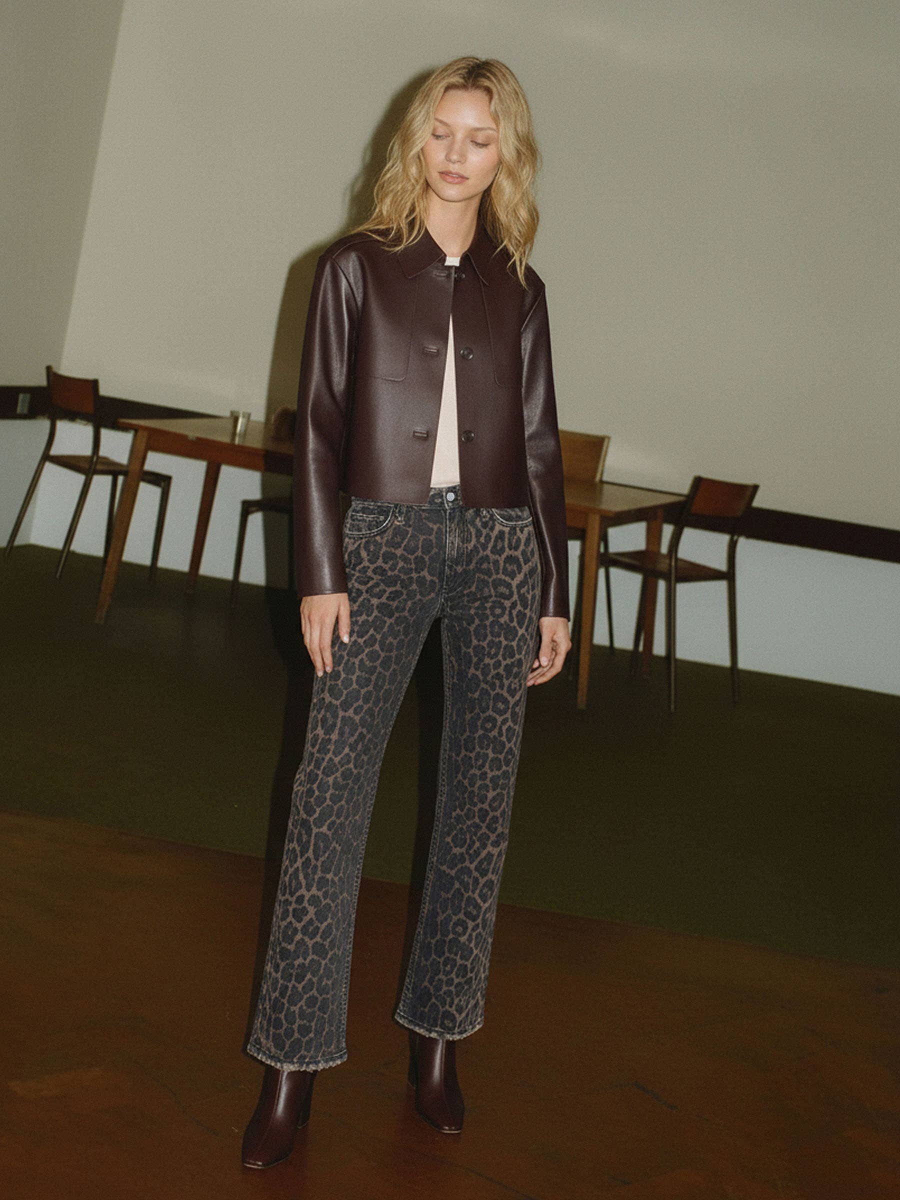 Woman wearing a brown leather jacket and leopard print pants in an indoor setting.