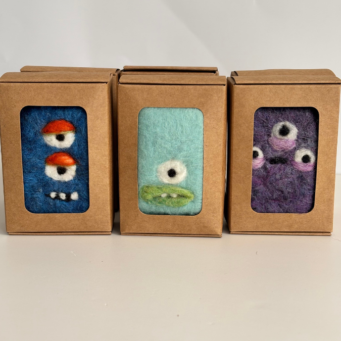 Three small felted creatures in cardboard boxes on a white background