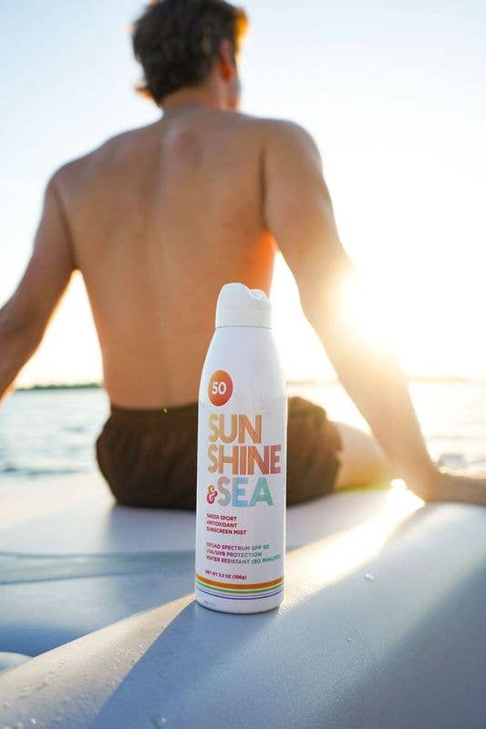 Person sitting on a beach with a 'Sun Shine & Sea' sunscreen spray can.