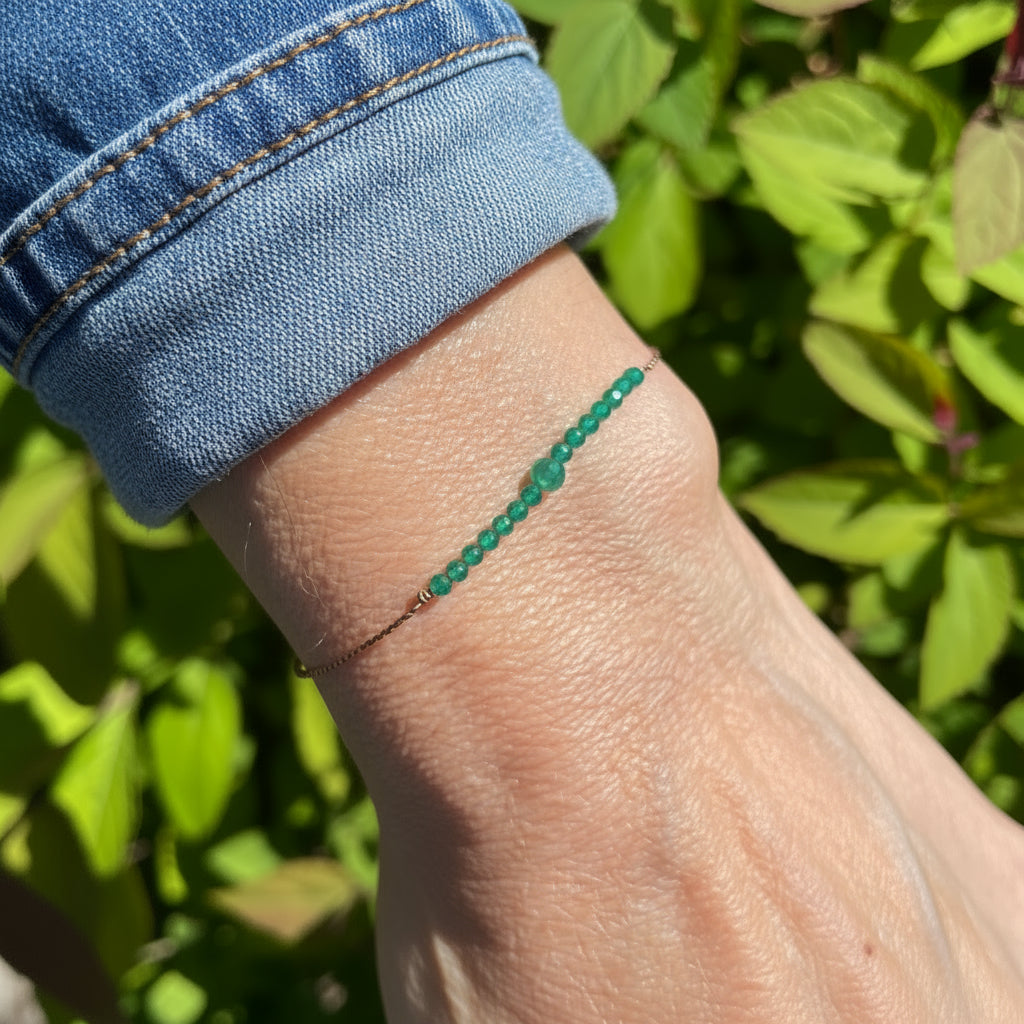 Green beaded bracelet on a wrist with a blurred green background