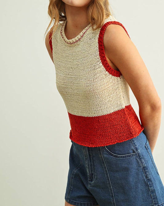 Woman wearing a sleeveless, color-blocked top with beige and red sections, paired with denim shorts on a plain background.