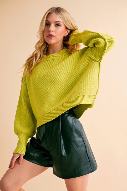 Woman wearing a bright yellow sweater and green shorts against a beige background