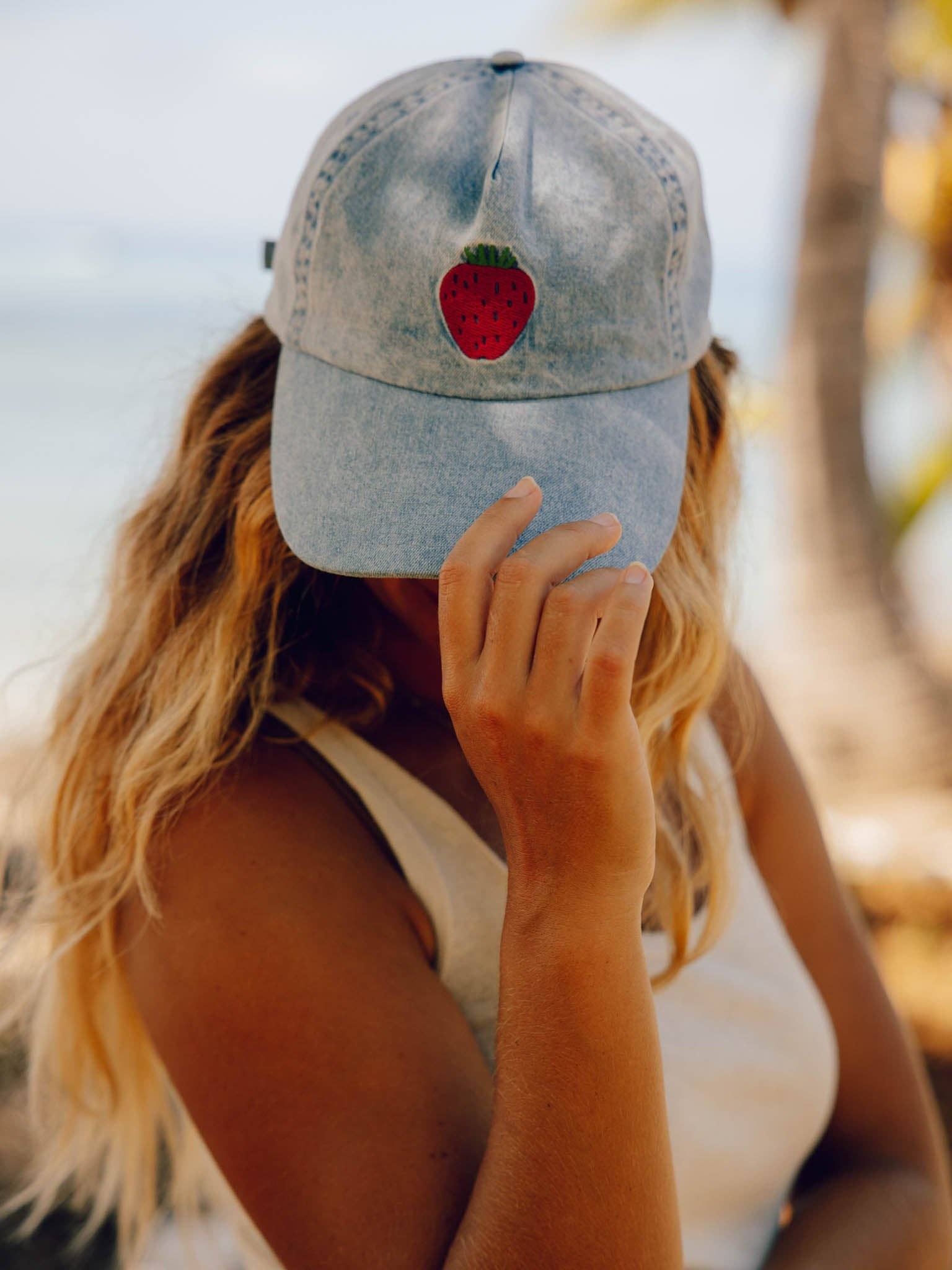 Person wearing a denim cap with a red strawberry patch outdoors