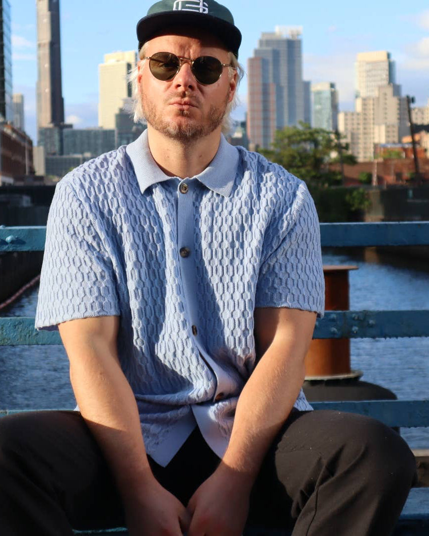 Man sitting on a blue railing with a cityscape in the background