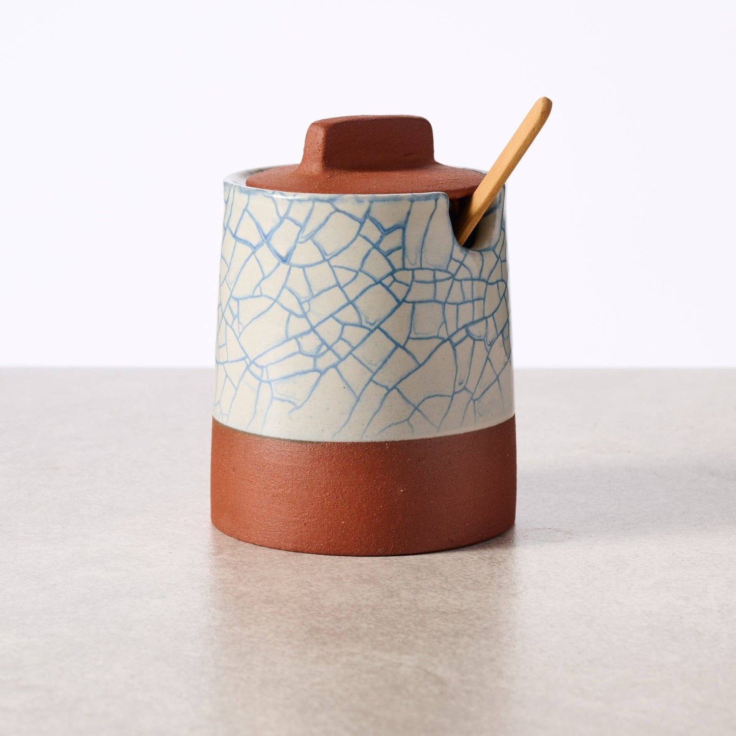 Ceramic container with textured lid and wooden spoon on a light background