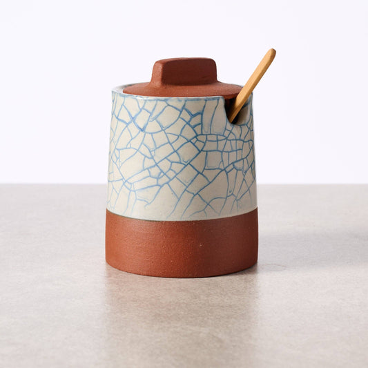 Ceramic container with textured lid and wooden spoon on a light background