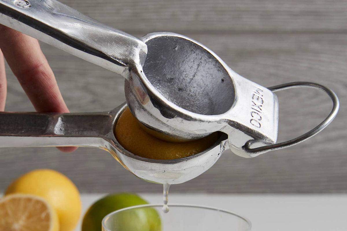 Metallic lemon squeezer being used to extract juice from a lemon on a neutral background.