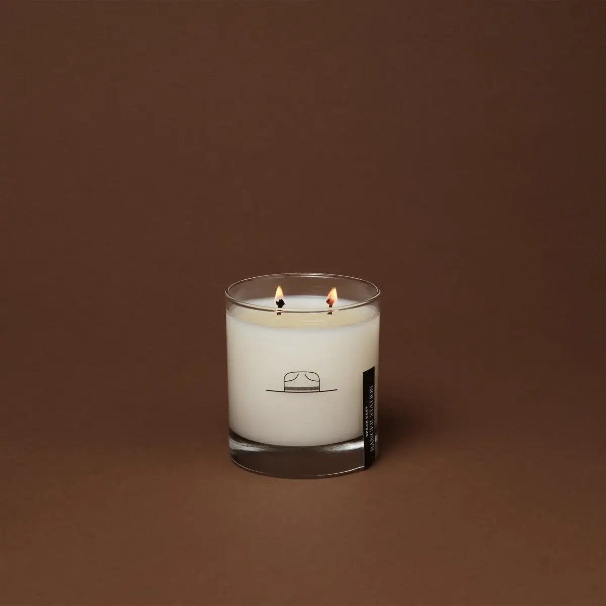 White candle in a glass container with a label on a brown background
