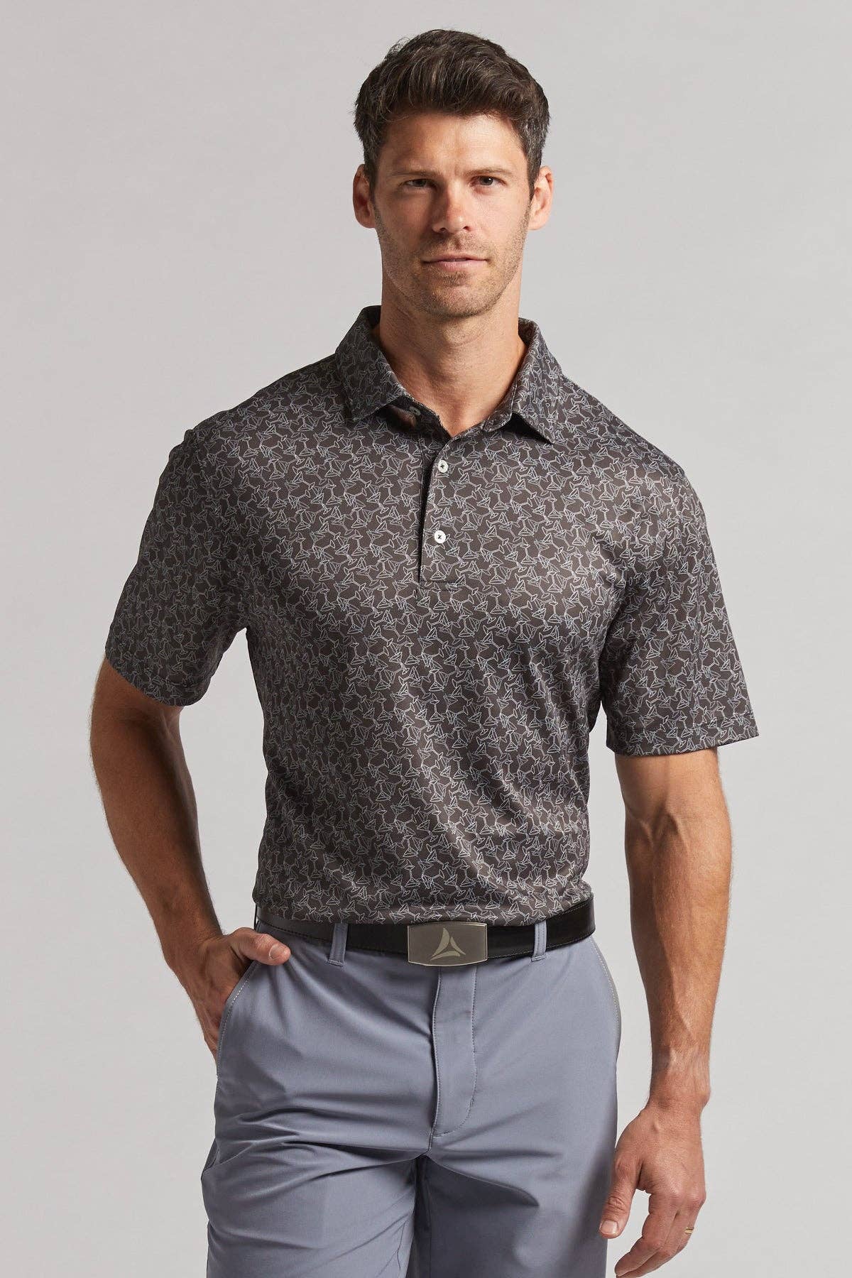 Man wearing a patterned polo shirt and light gray pants on a plain background