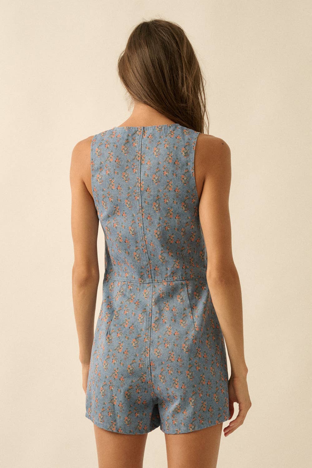 Woman wearing a blue floral romper against a beige background