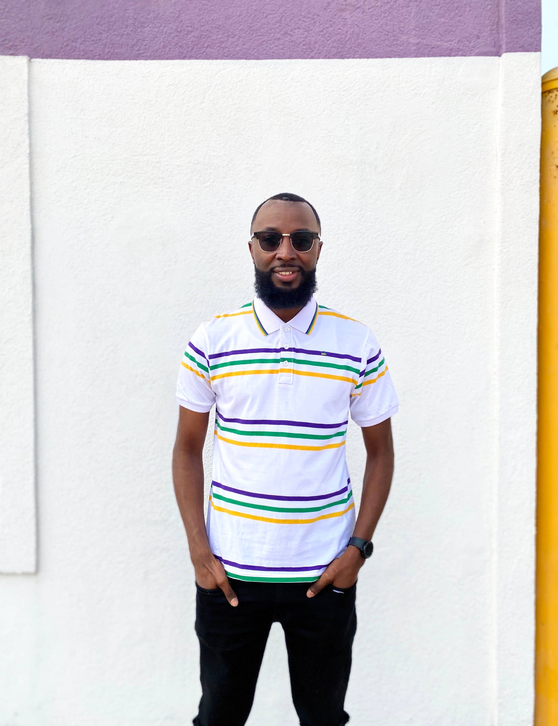 Man wearing a white polo shirt with colorful stripes standing against a white wall.