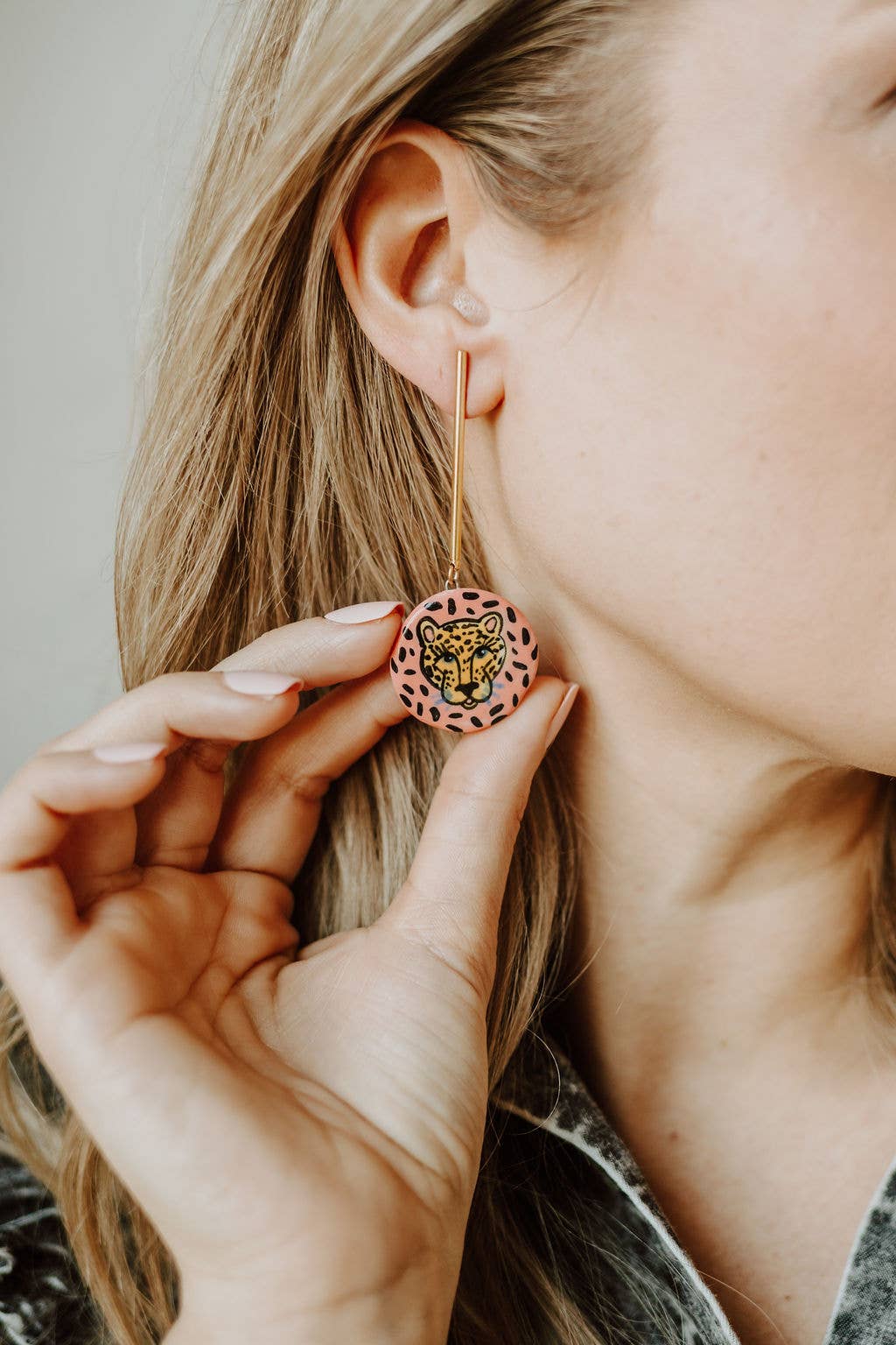 Person wearing a pink lion-shaped earring with a neutral background