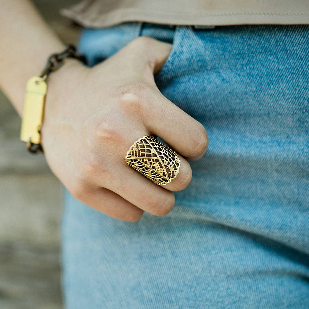 Hand wearing a gold ring with intricate design, blue jeans, and yellow bracelet.