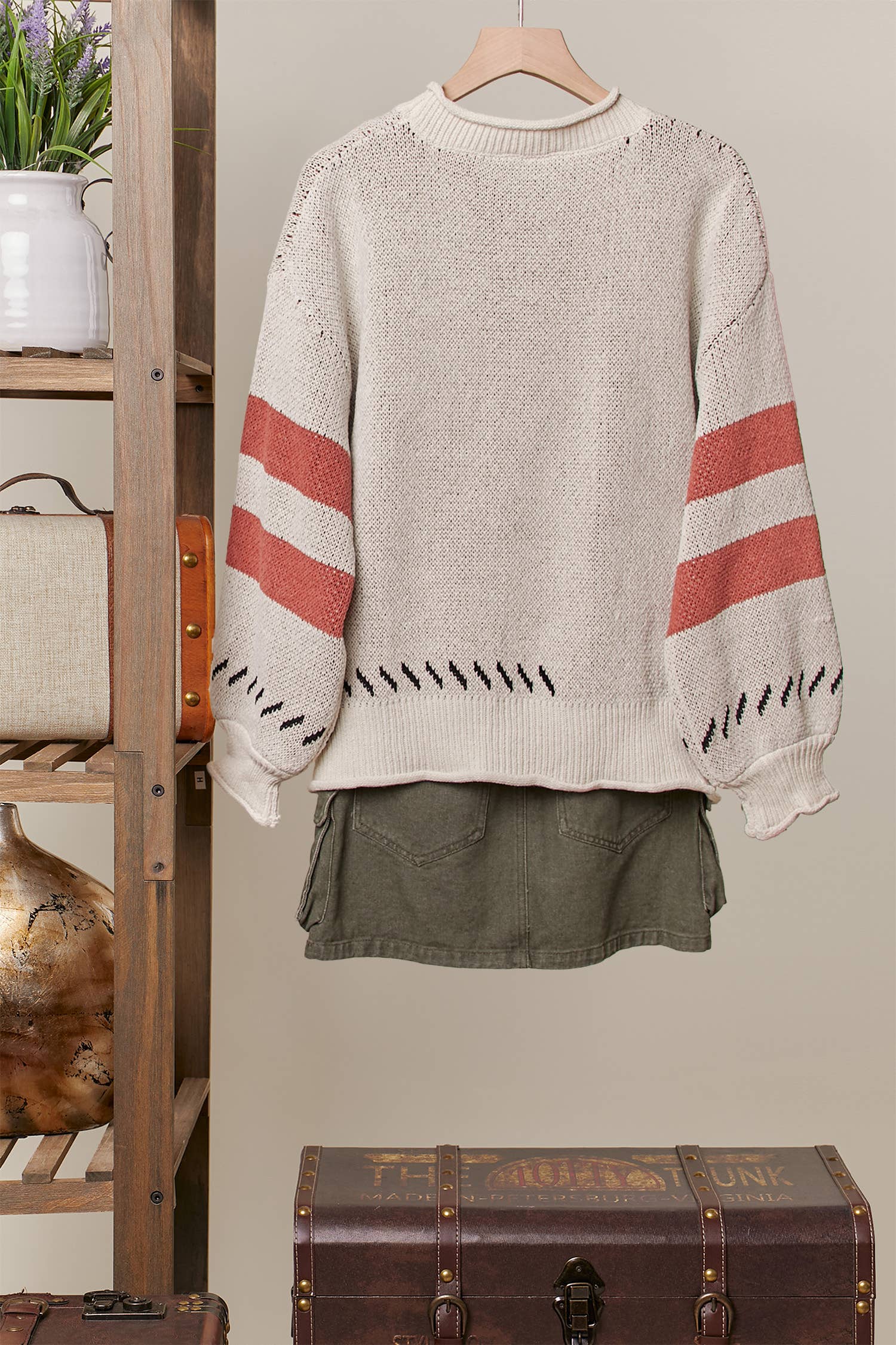 Beige sweater with red and black stripes on a hanger against a neutral wall.