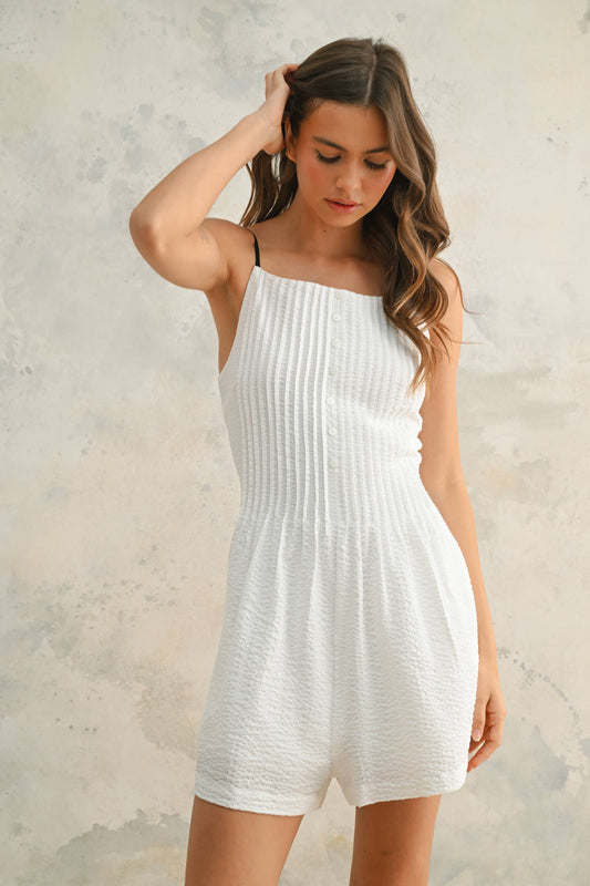 Woman wearing a white ribbed dress against a textured wall.