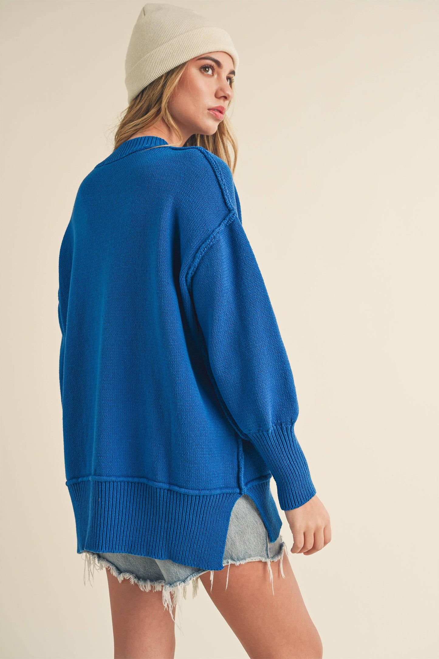 Woman wearing a blue sweater and denim shorts on a beige background