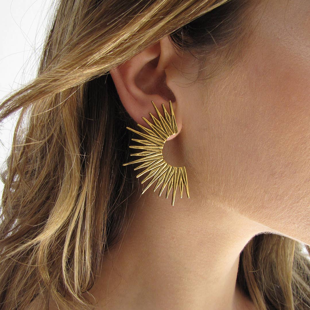 Close-up of a person wearing a gold sunburst earring.