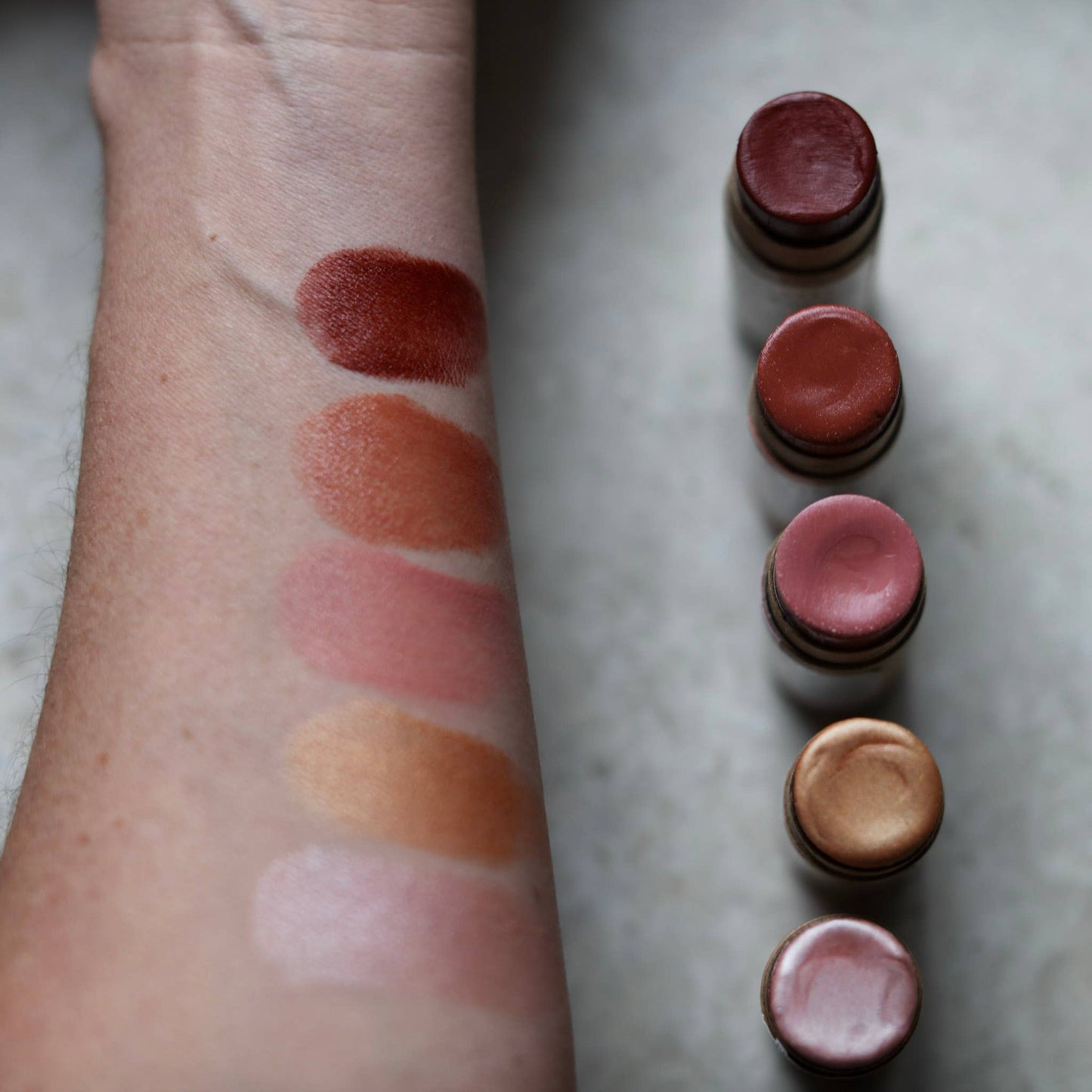 Lipstick swatches on a person's arm next to lipstick tubes on a marble surface
