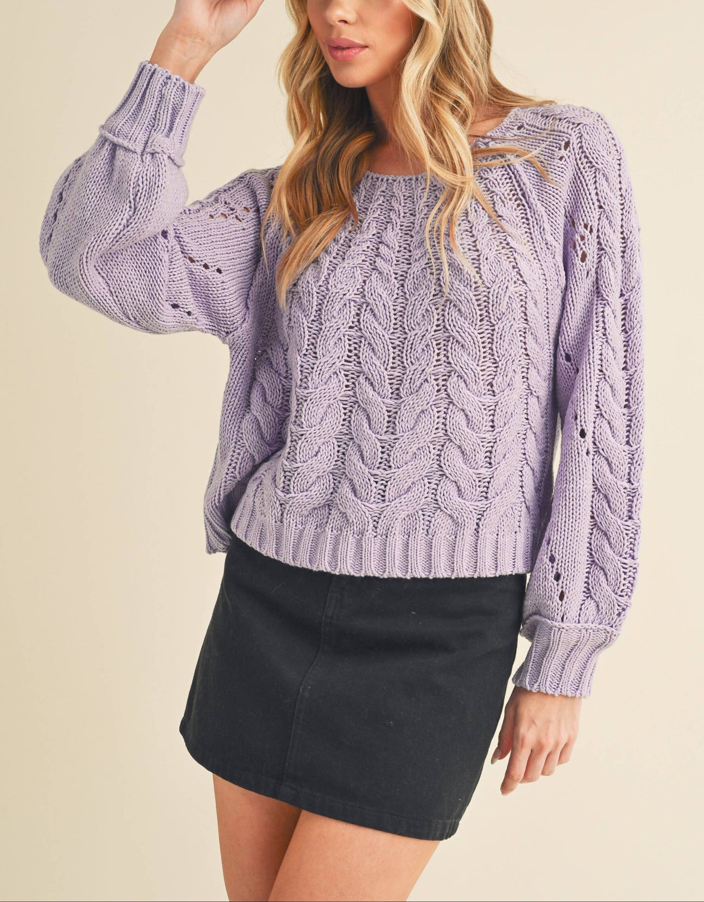 Woman wearing a purple cable knit sweater and black cap on a beige background
