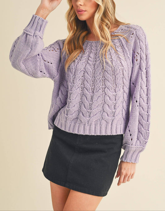 Woman wearing a purple cable knit sweater and black cap on a beige background