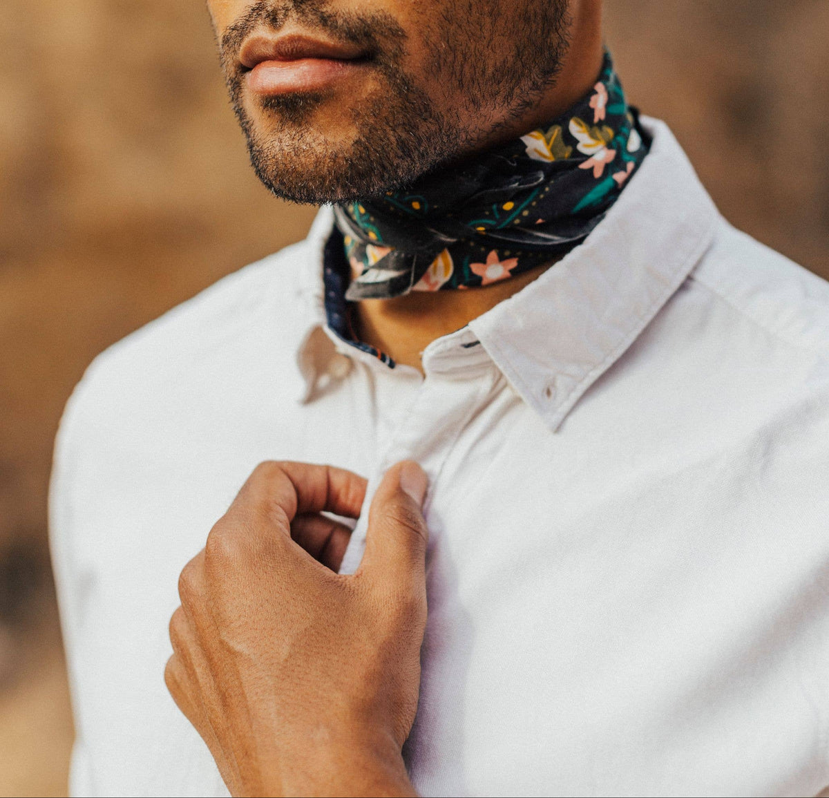 Man wearing a white shirt and floral neck scarf with a blurred natural background